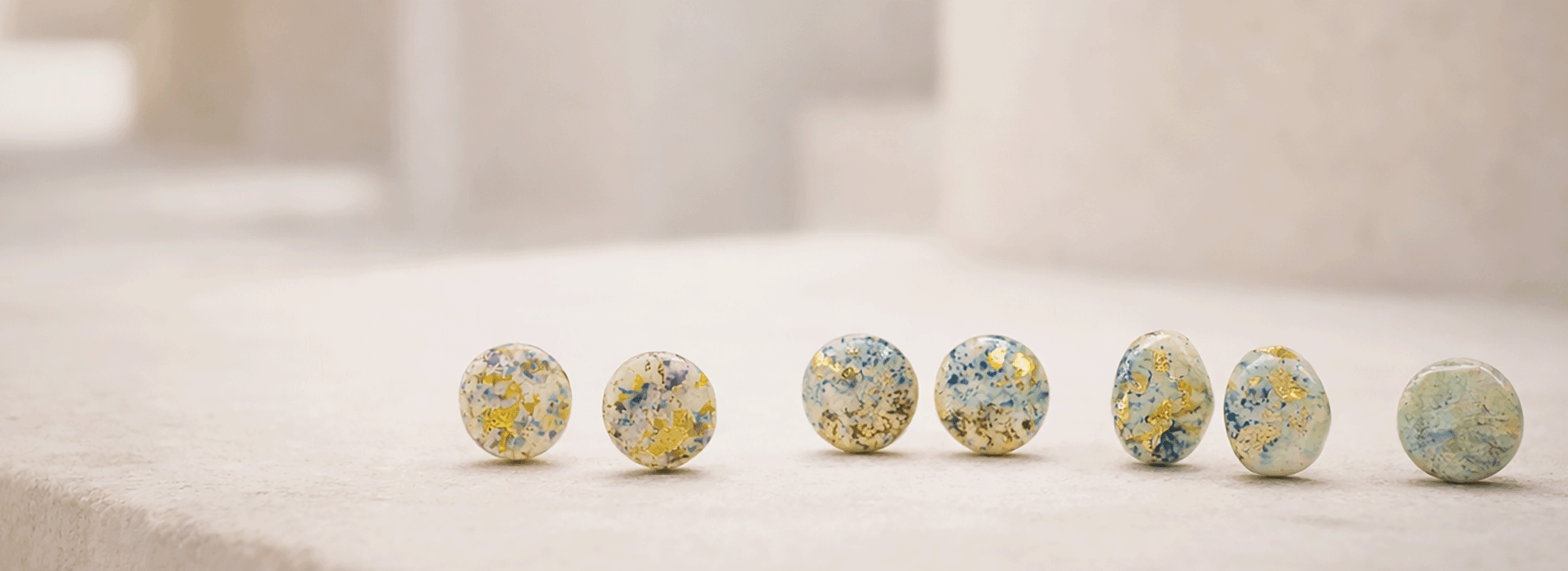 pure_form_ceramic_stud_earrings_luxury_campaign_minimalist_mediterranean_architecture_honed_limestone_surface_soft_natural_daylight_hand_painted_textured_round_blue_green_gold_speckled_designs_medium_format_photography