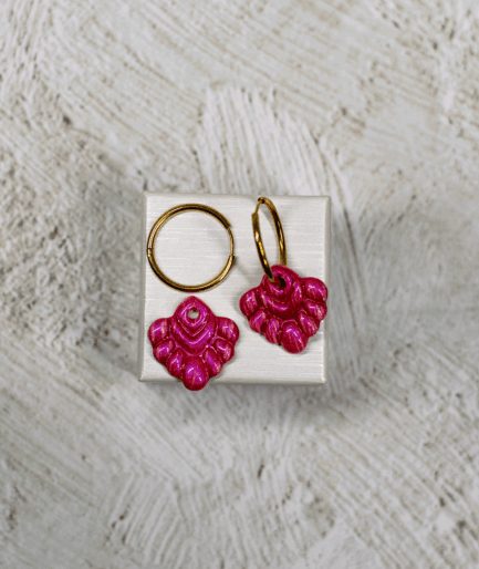 coral pink hoop earrings with raised rounded details and glossy fuchsia charms on a white display stand