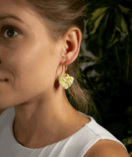 woman wearing mint coral hoop earrings with pale green textured charms and gold-tone hoops