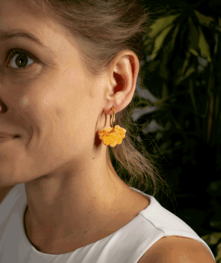woman wearing orange shell hoop earrings with textured polymer clay charms and gold-tone hoops