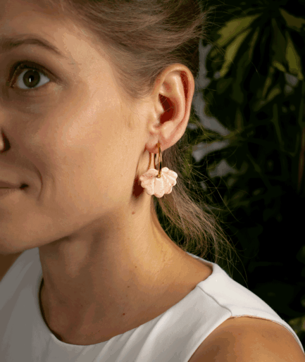 woman wearing peach shell hoop earrings with sculpted blush pink polymer clay charms and gold-tone hoops