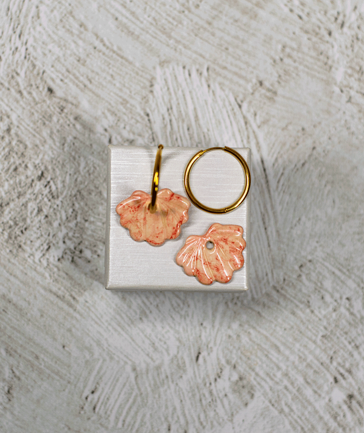 charm_10_c1 peach shell hoop earrings with glossy peach and coral-speckled seashell charms on a white display stand