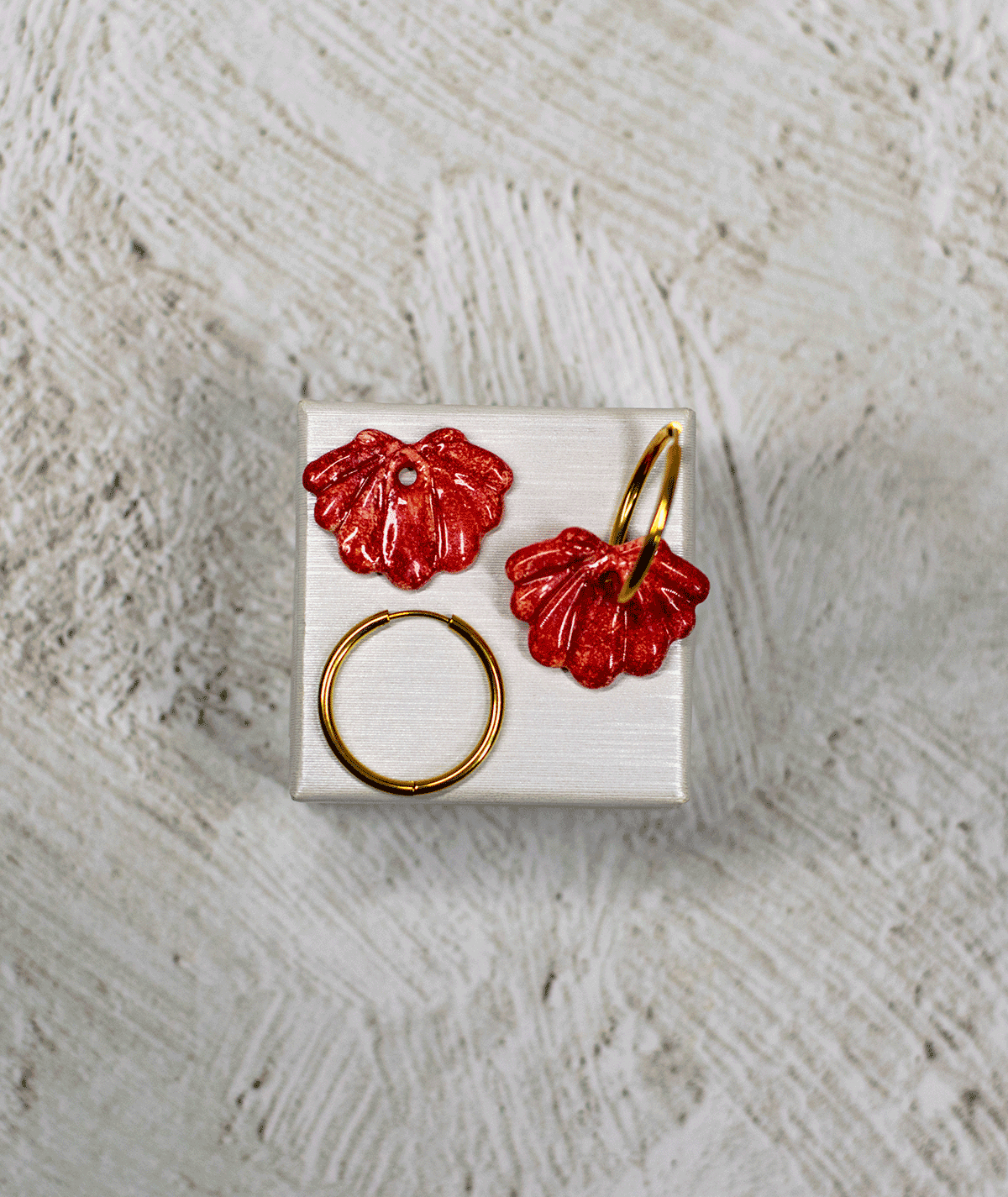 charm_11_c1 red shell hoop earrings with sculpted ridges and glossy speckled polymer clay charms on a white display stand