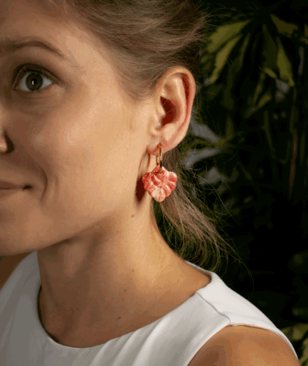 woman wearing coral red hoop earrings with sculpted pink and red polymer clay charms and gold-tone hoops
