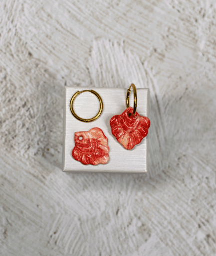 coral red hoop earrings with glossy marbled polymer clay charms in coral red and cream on a white display stand