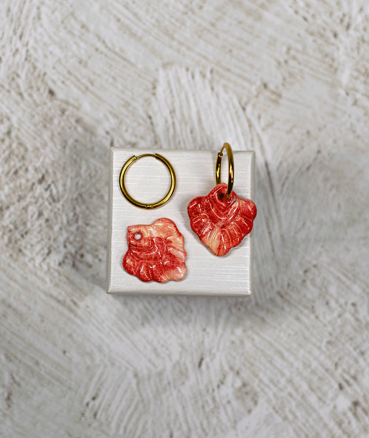 charm_14_c1 coral red hoop earrings with glossy marbled polymer clay charms in coral red and cream on a white display stand