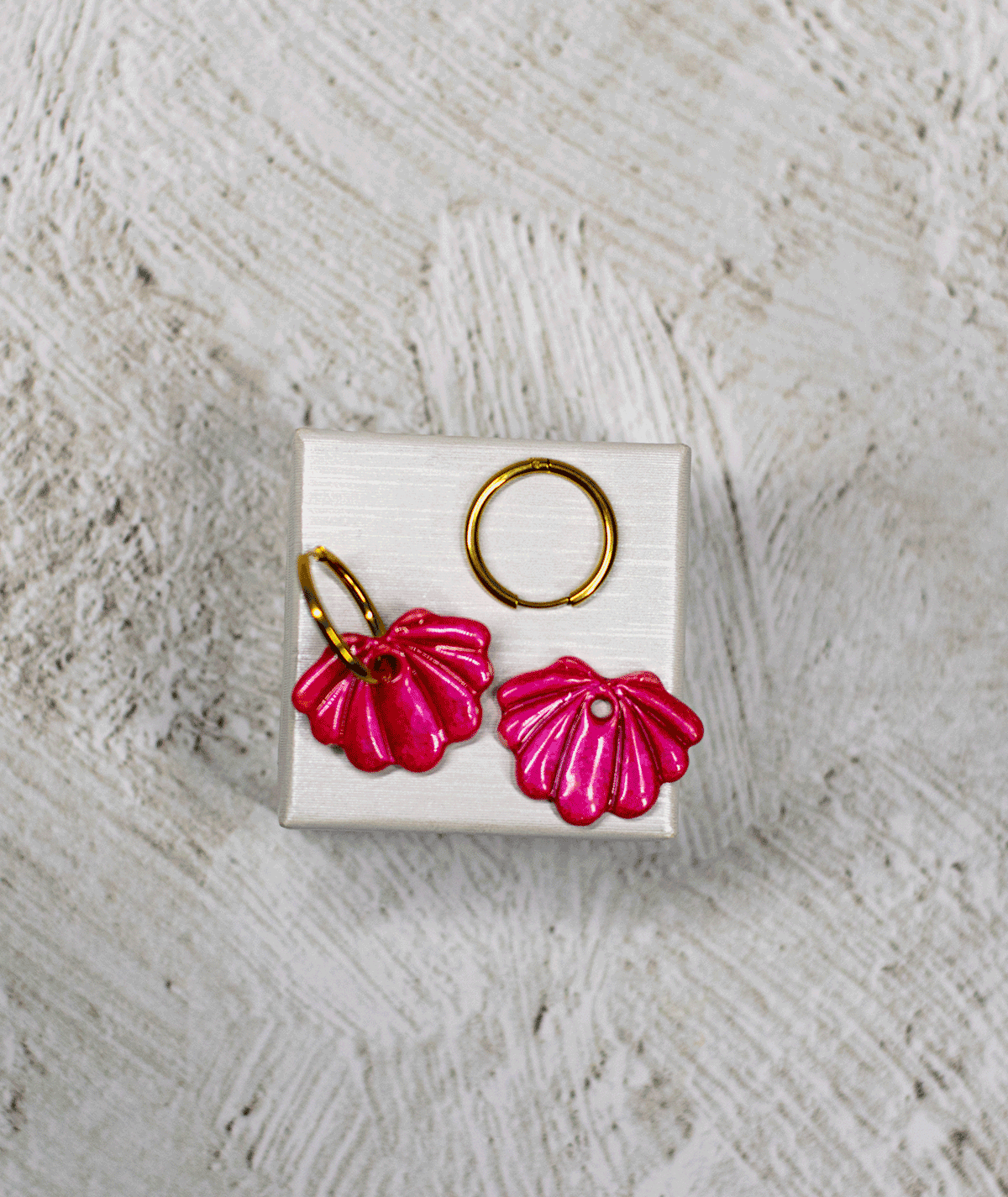 charm_15_c1 raspberry shell hoop earrings with metallic pink polymer clay charms and raised ridges on a white display stand