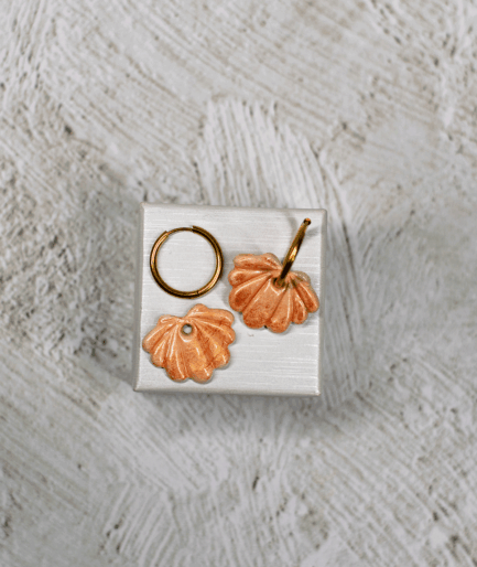 apricot shell hoop earrings with sculpted ridges and pearlescent peach polymer clay charms on a white display stand