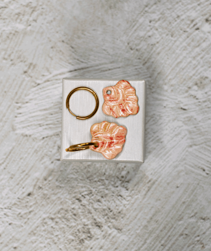 ivory coral hoop earrings with glossy polymer clay charms in creamy white, peach and red on a white display stand