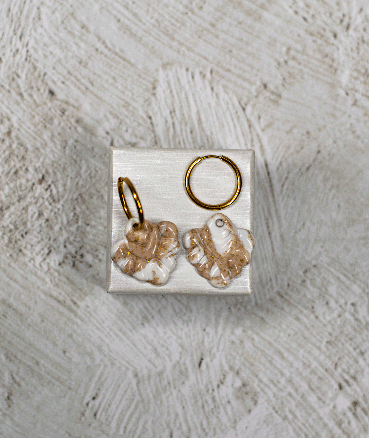 charm_20_c1 beige coral hoop earrings with glossy ivory and sandy beige marbled polymer clay charms on a white display stand
